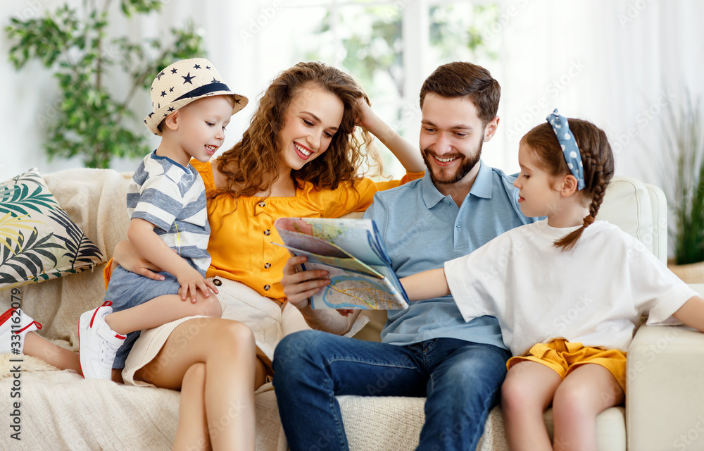 Cheerful parents with kids reading map on sofa at home.