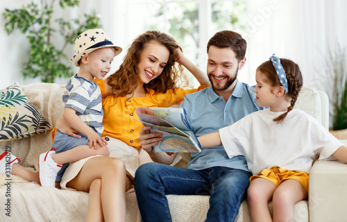 Cheerful parents with kids reading map on sofa at home.