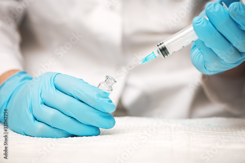 Doctor or nurse hands in blue gloves holding syringe and vaccine injection.