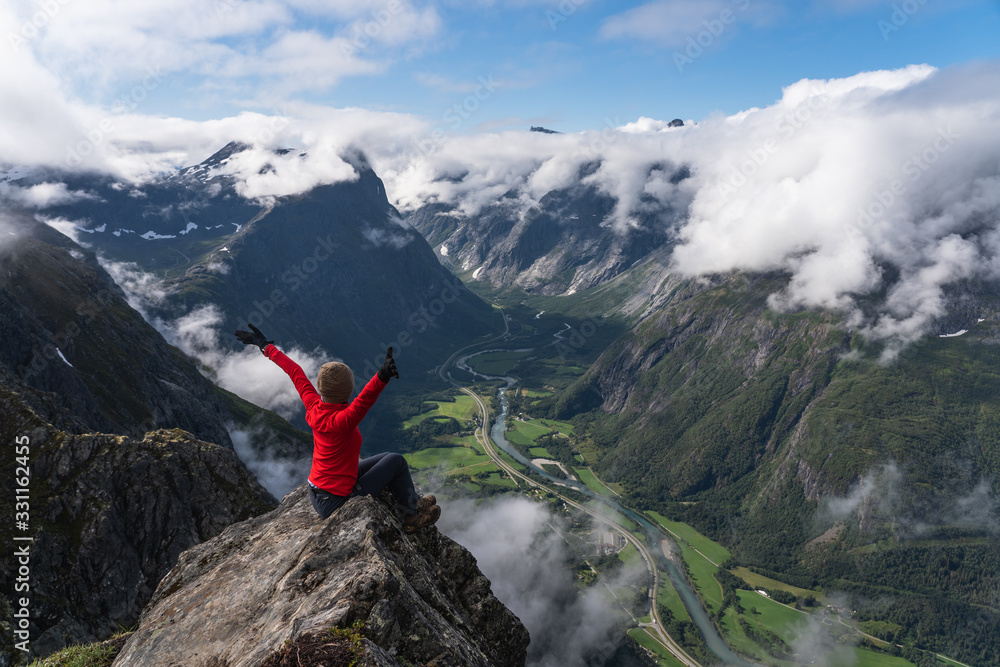 A woman hiker sitting on rock looking at mountain, Romsdalseggen trail, Norway, Scandinavia