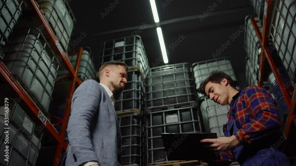 From below tracking shot of inspector signing report and shaking hands with material handler in industrial storage From below tracking shot of inspector signing report and shaking hands with material handler in industrial storage