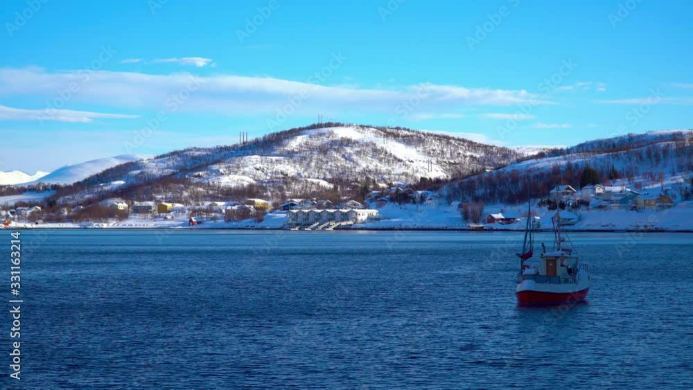 Kaldfjord, Troms og Finnmark / Norway - March 4th, 2020: Small fishing boat with small wooden houses on the banks of a fjord Kaldfjord, Troms og Finnmark / Norway - March 4th, 2020: Small fishing boat with small wooden houses on the banks of a fjord