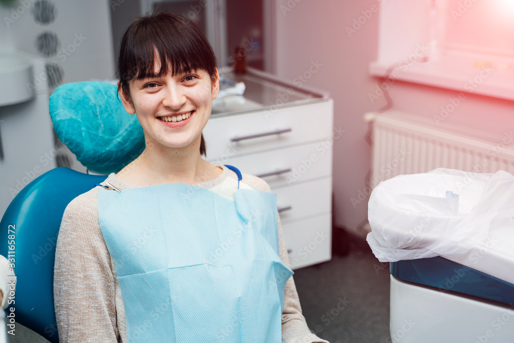 Fototapeta premium Young female patient visiting dentist office. Beautiful smiling woman with healthy straight white teeth sitting at dental chair. Dental clinic.Stomatology