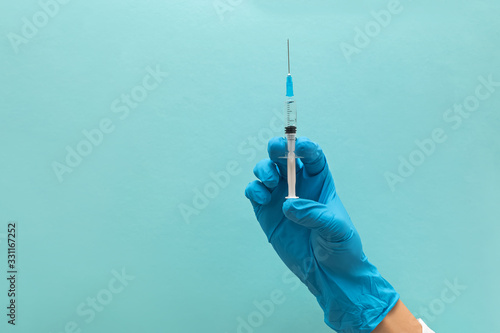 Hand in blue gloves holding syringe isolated on blue background photo