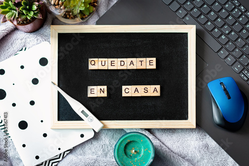 Spanish words quedate en casa made of wooden blocks, concept of self quarantine at home as preventative measure against virus outbreak. Flat lay, laptop, note books, staying at home during emergency photo