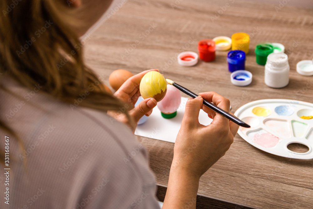 easter mood. close up young woman hands painting easter eggs with brush and gouache in pastel colors over wooden table at home easter mood. close up young woman hands painting easter eggs with brush and gouache in pastel colors over wooden table at home