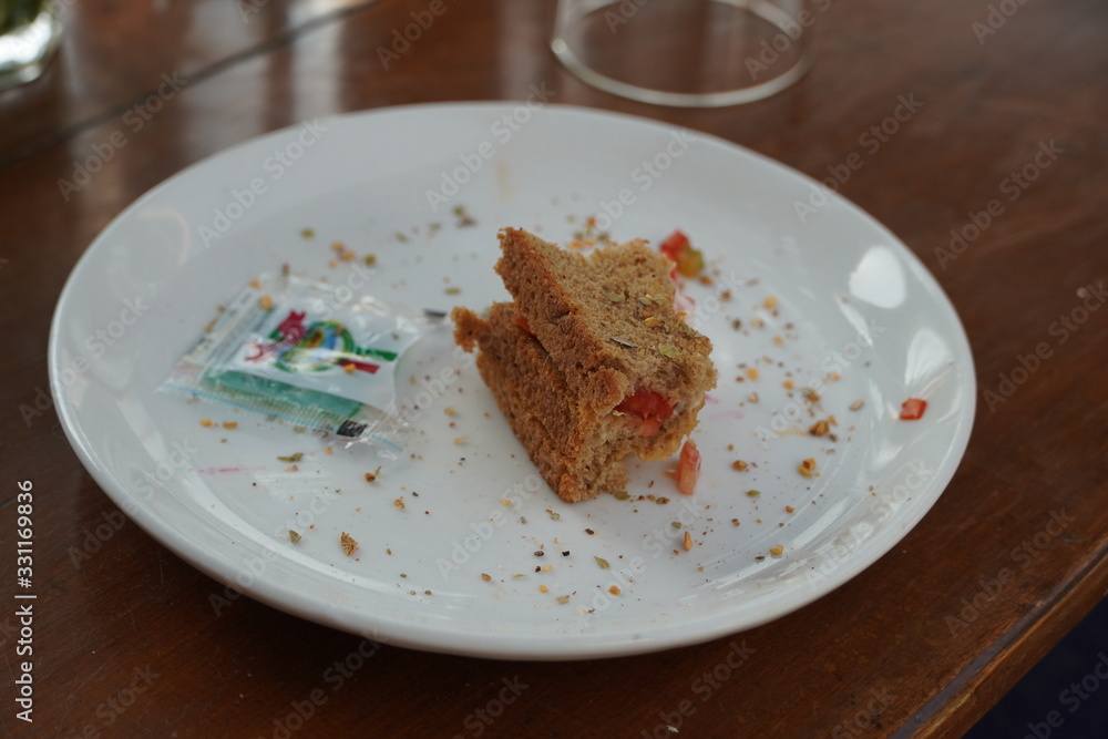 Last bite of a vegetable sandwich kept on plate. Side view shot of a piece bread with tomato with the last bit. Last bite of a vegetable sandwich kept on plate. Side view shot of a piece bread with tomato with the last bit.