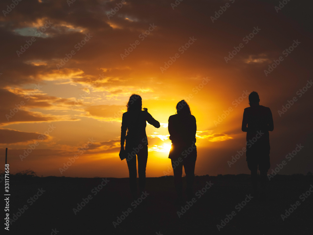 Three friends walking to the sunset