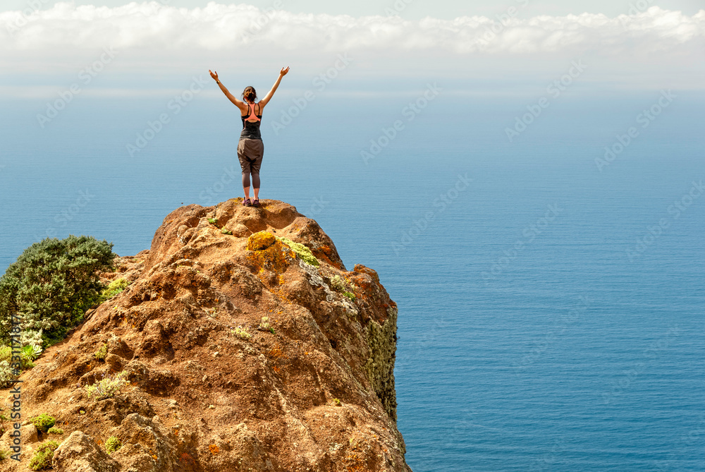 Woman standing with the arms open in a cliff looking to the sea Woman standing with the arms open in a cliff looking to the sea