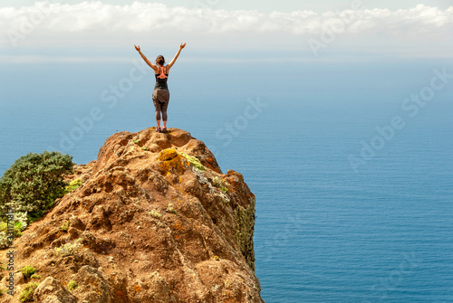 Woman standing with the arms open in a cliff looking to the sea