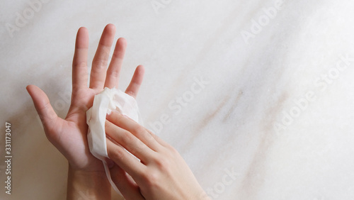 Right hand wiping left hand with a piece of wet tissue, with copy space on the right. Top view.