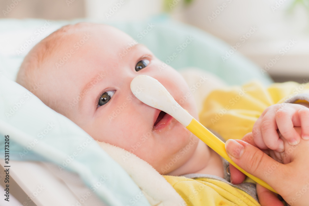 Introduction of complementary foods. The baby will eat children's nutrition. Toddler with a spoon in a high chair for feeding. Introduction of complementary foods. The baby will eat children's nutrition. Toddler with a spoon in a high chair for feeding.