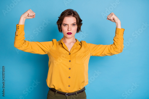 Girls power. Photo of pretty serious lady hold raise biceps two hands showing perfect biceps after gym training wear yellow shirt green pants isolated bright blue color background