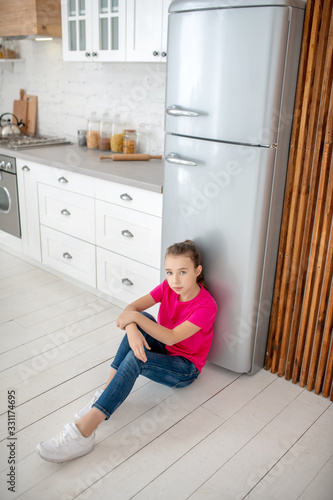 Girl in bright tshirt sitting on the floor near the fridge