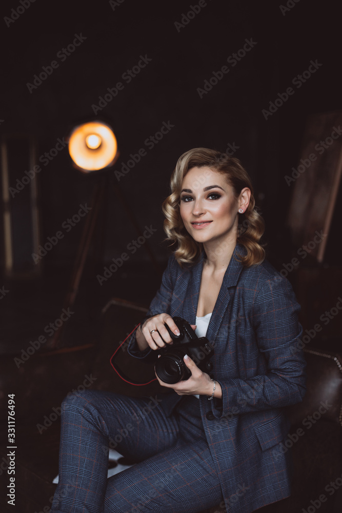 Portrait of a confident beautiful business woman in a suit on a dark background holds a camera in her hands. The concept of gender equality. Strong independent woman. Soft selective focus.