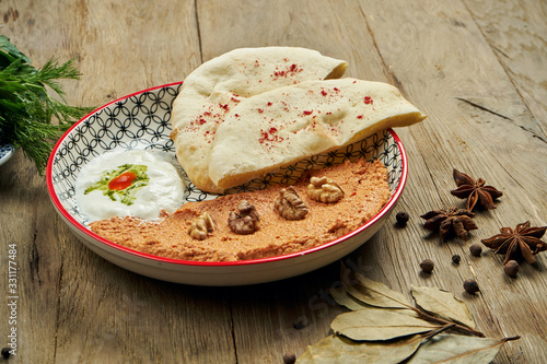 Muhammara is a classic eastren dish. baked pepper and walnut puree with Bazlama and yogurt in a ceramic plate on a wooden background. photo