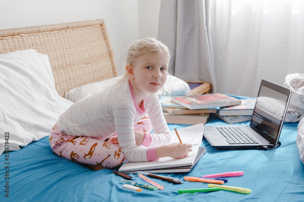 Caucasian girl child sitting in a bed and learning online on laptop Internet. Virtual class lesson on video during self isolation at home. Distant remote video education. Modern school study for kids. Caucasian girl child sitting in a bed and learning online on laptop Internet. Virtual class lesson on video during self isolation at home. Distant remote video education. Modern school study for kids.