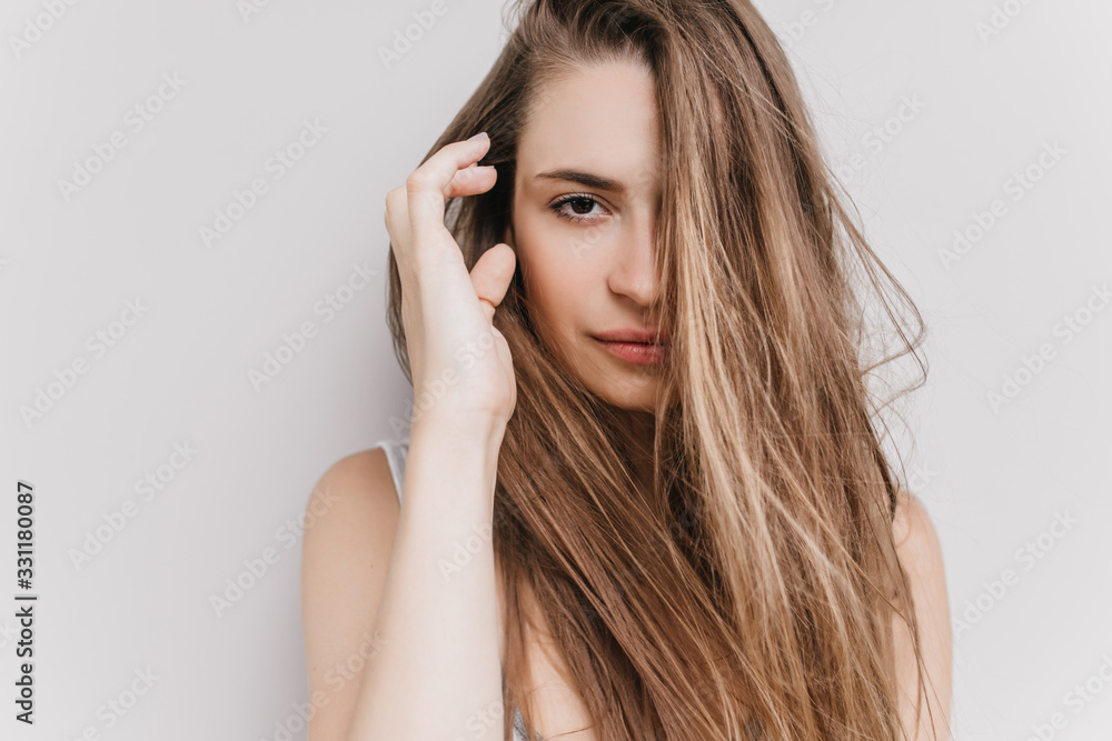 Happy dark-eyed girl posing in morning on light background. Studio shot of enchanting caucasian female model touching her dark hair.