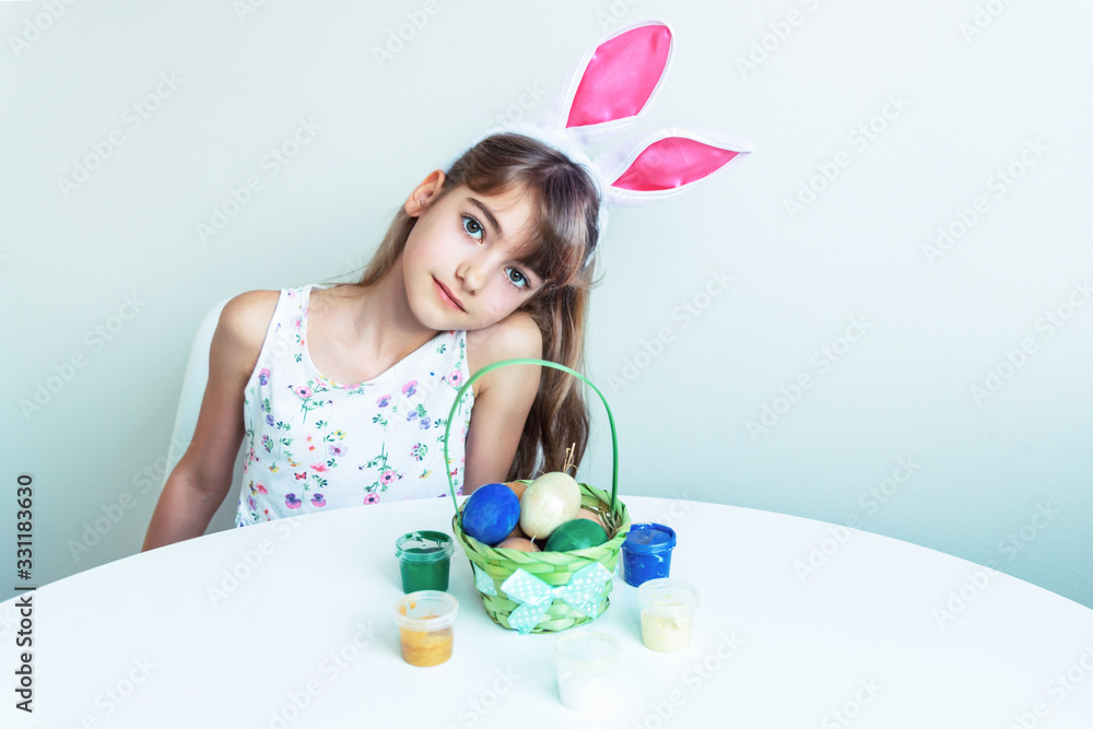 Cute little girl with bunny ears paints eggs at a white table. Easter concept Cute little girl with bunny ears paints eggs at a white table. Easter concept