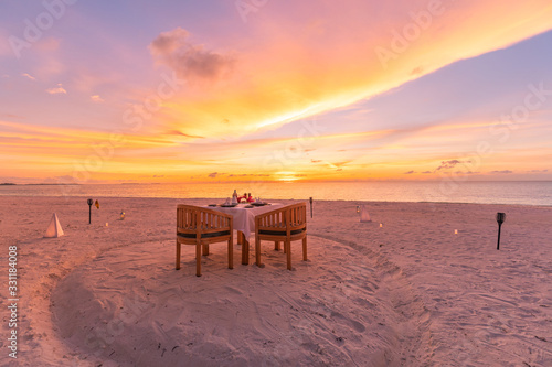 Romantic dinner on the beach with sunset. Couple honeymoon or anniversary dinner at the beach. Summer sunset landscape with beach dinner table and chairs
