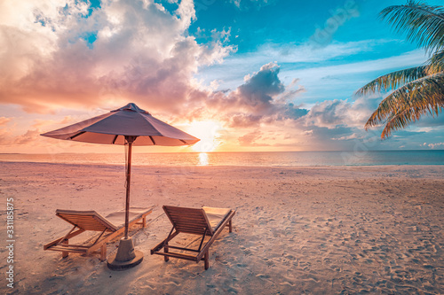 Fototapeta Naklejka Na Ścianę i Meble -  Beautiful tropical sunset scenery, two sun beds, loungers, umbrella under palm tree. White sand, sea view with horizon, colorful twilight sky, calmness and relaxation. Inspirational beach resort hotel