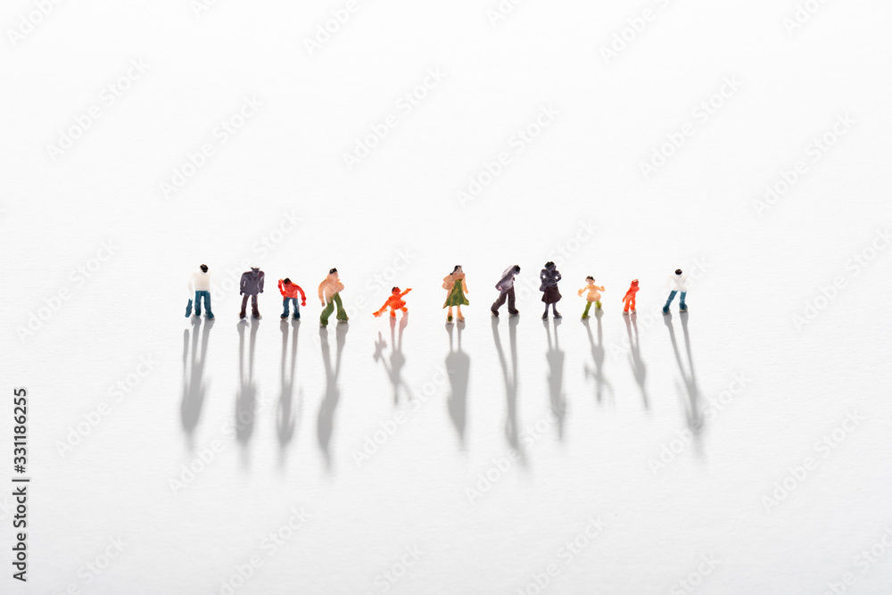 High angle view of row of plastic people figures with shadow on white surface High angle view of row of plastic people figures with shadow on white surface