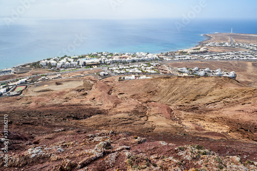 Der Vulkan Montana Roja de Playa Blanca mit einer Höhe von 194m und im Hintergrund die Südwestspitze der Atlantikküste mit dem Leuchtturm auf der Kanareninsel Lanzarote