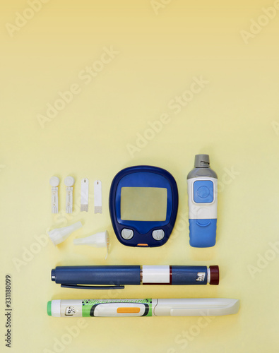 Diabetic kit: glucometer, test strips, lancet, insulin pens, metformin tablets. Top view, yellow background, empty space.