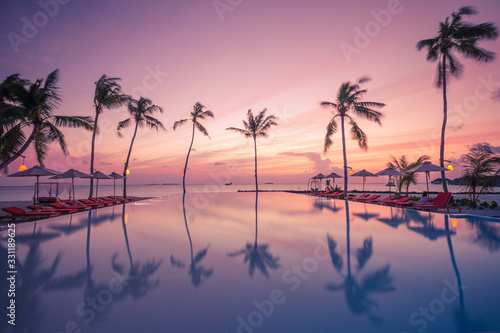 Fototapeta Naklejka Na Ścianę i Meble -  Luxury sunset over infinity pool in a summer beachfront hotel resort at tropical landscape. Tranquil beach holiday vacation background mood. Amazing island sunset beach view, palms swimming pool