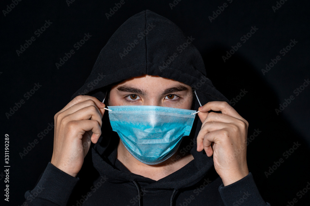 teenager in a hood puts on a disposable mask in the dark. teenager in a hood puts on a disposable mask in the dark.