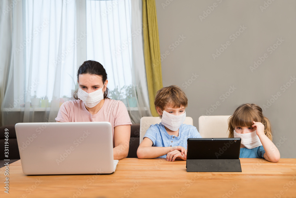 Mother and two kids wearing medical face mask together at home. quarantine. Corona Virus. Mom Work on the Internet on a laptop and kids study online at home. Mother and two kids wearing medical face mask together at home. quarantine. Corona Virus. Mom Work on the Internet on a laptop and kids study online at home.