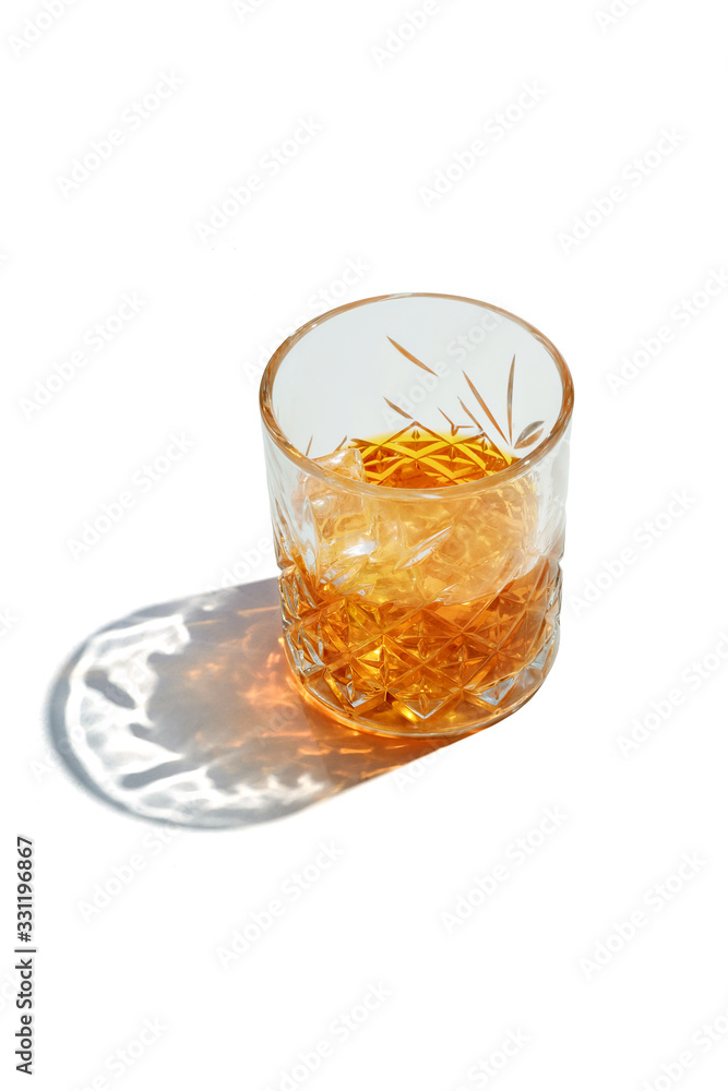 Old Fashioned Whiskey is contained in a crystal lowball glass with ice cubes. The showy illustrative picture is made on the white backdrop. Old Fashioned Whiskey is contained in a crystal lowball glass with ice cubes. The showy illustrative picture is made on the white backdrop.