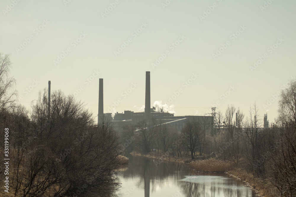 Wolno płynąca rzeka na tle kominów fabryki.