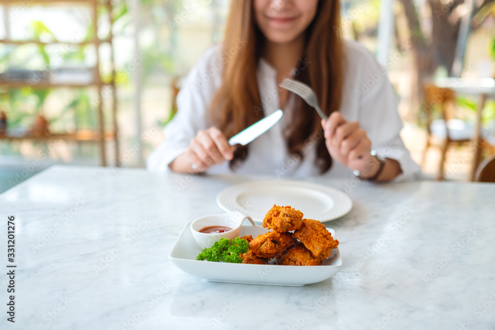 Closeup image of a beautiful asian woman using knife and fork to eat fried chicken in restaurant Closeup image of a beautiful asian woman using knife and fork to eat fried chicken in restaurant
