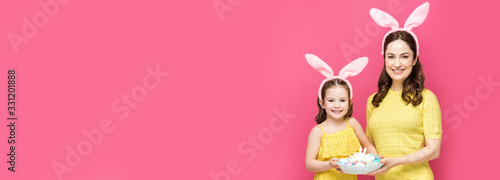 Canvas Print panoramic shot of happy mother and daughter in bunny ears holding easter eggs is