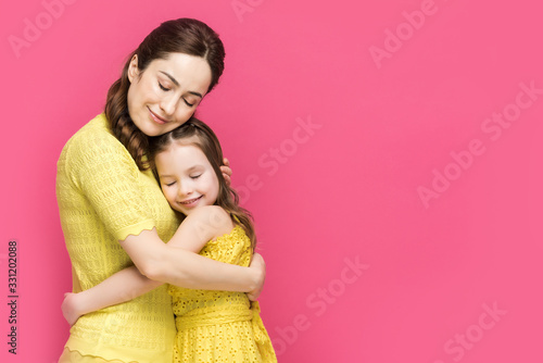 cheerful mother and daughter with closed eyes hugging isolated on pink