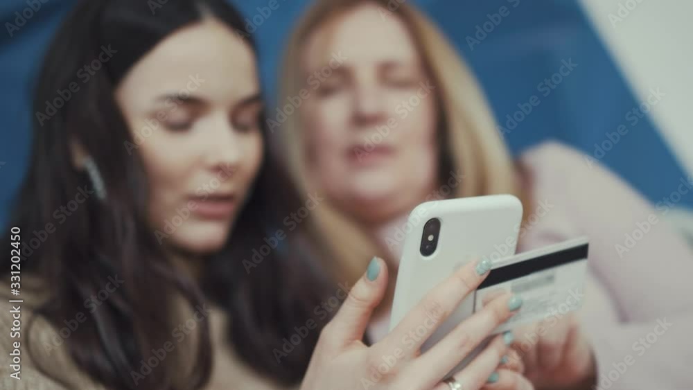 advanced blonde mother and brunette daughter pay online purchase using modern smartphone and credit card blurry close view advanced blonde mother and brunette daughter pay online purchase using modern smartphone and credit card blurry close view