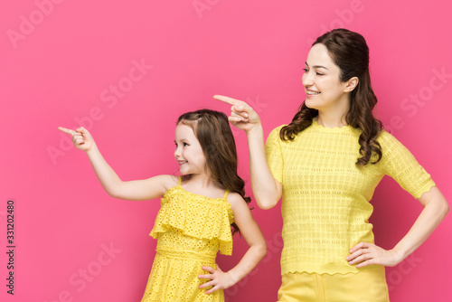 happy mother and kid pointing with fingers isolated on pink