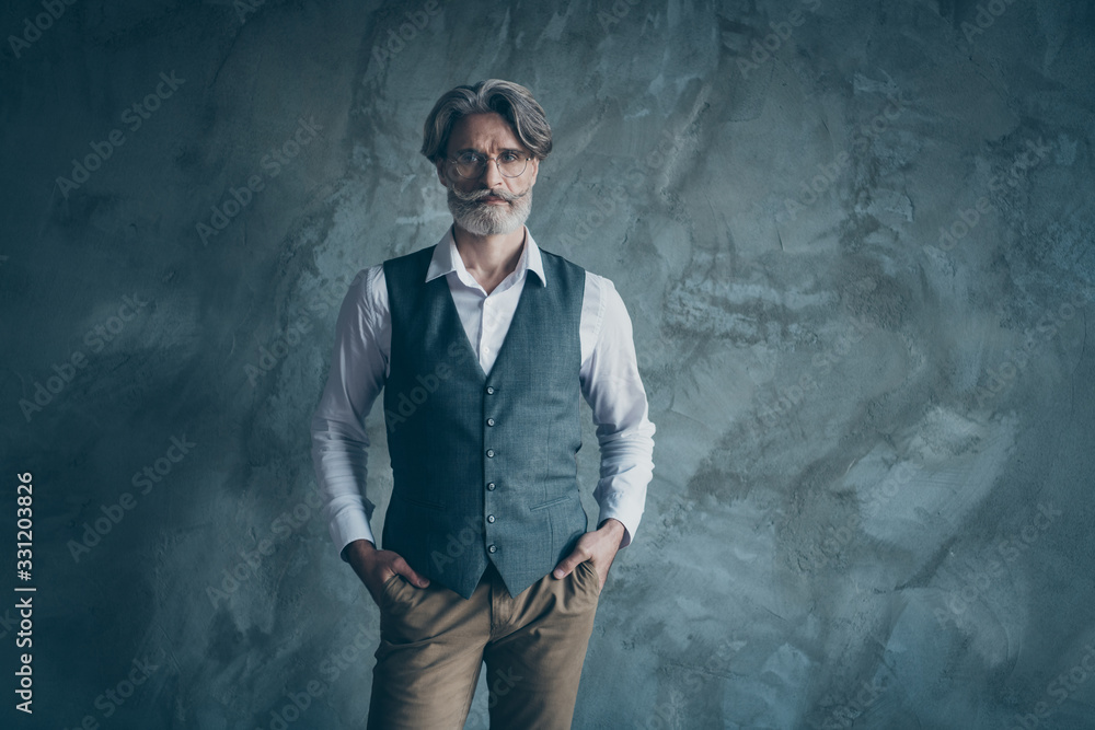 Photo of aged macho business man standing calm not smiling serious wear specs office white shirt waistcoat trousers isolated over concrete grey color wall background Photo of aged macho business man standing calm not smiling serious wear specs office white shirt waistcoat trousers isolated over concrete grey color wall background