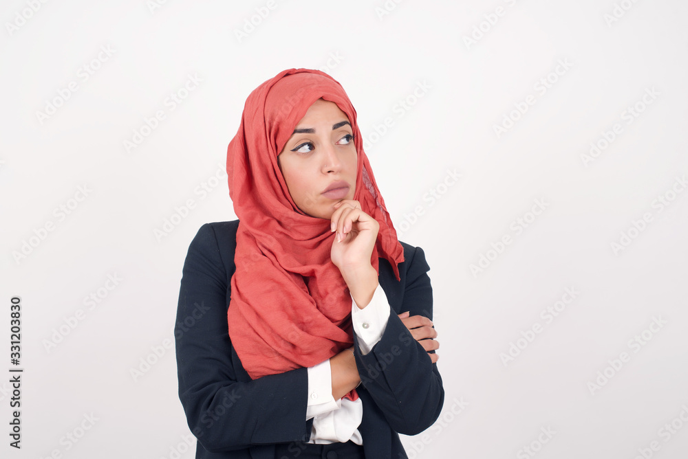 Portrait of thoughtful woman keeps hand under chin, looks away trying to remember something or listens something with interest, dressed casually, poses indoors. Youth concept. Portrait of thoughtful woman keeps hand under chin, looks away trying to remember something or listens something with interest, dressed casually, poses indoors. Youth concept.