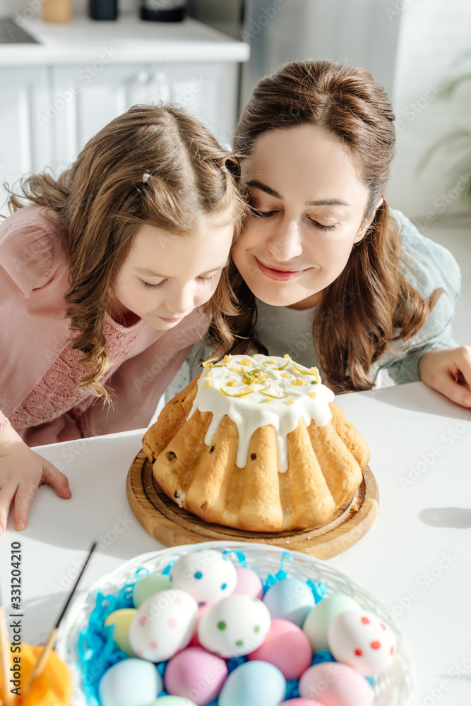 selective focus of happy mother and daughter smelling easter cake near painted chicken eggs