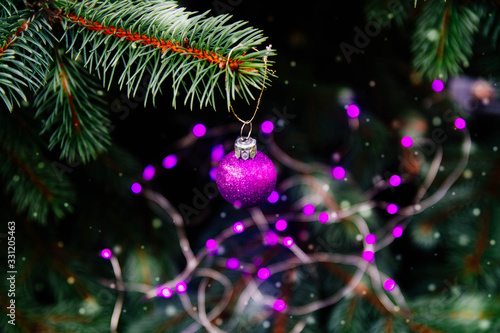 The tree is decorated for Christmas with a purple garland with bulbs, a ball. Copy space. Glare, light, on the Christmas tree. Beautiful background of natural spruce. It's snowing, 