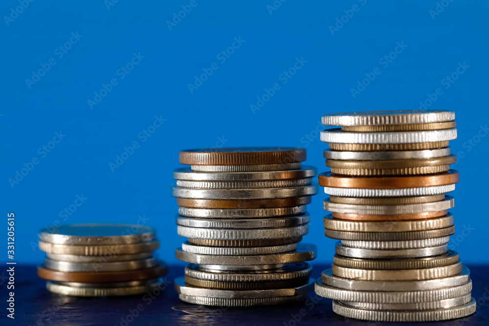 Three piles of various coins shown on blue background Three piles of various coins shown on blue background