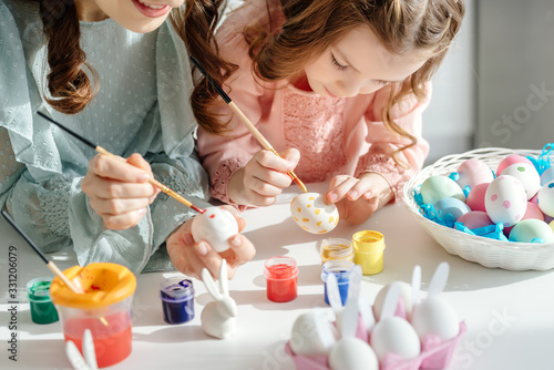 Foto selective focus of happy mother and cute daughter painting easter eggs near deco