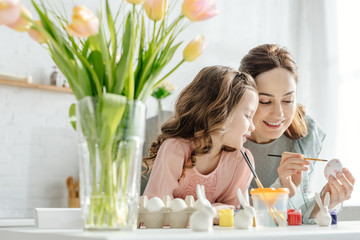 selective focus of happy mother and kid painting easter eggs