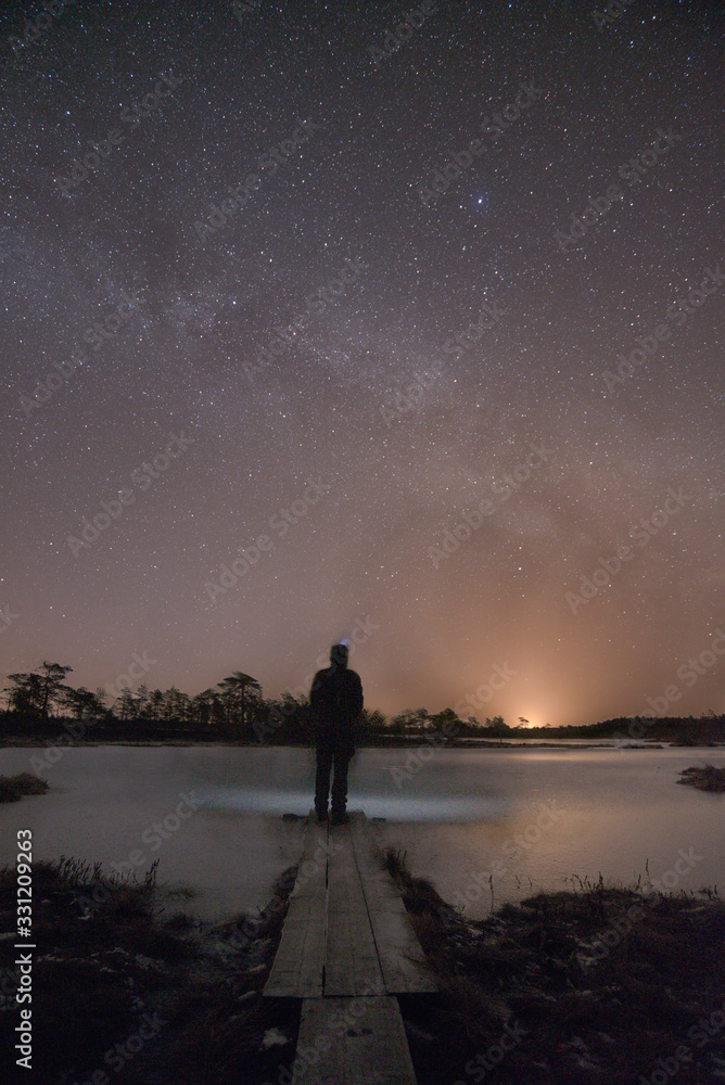 Figure on path in bog under starry night sky and Milky Way