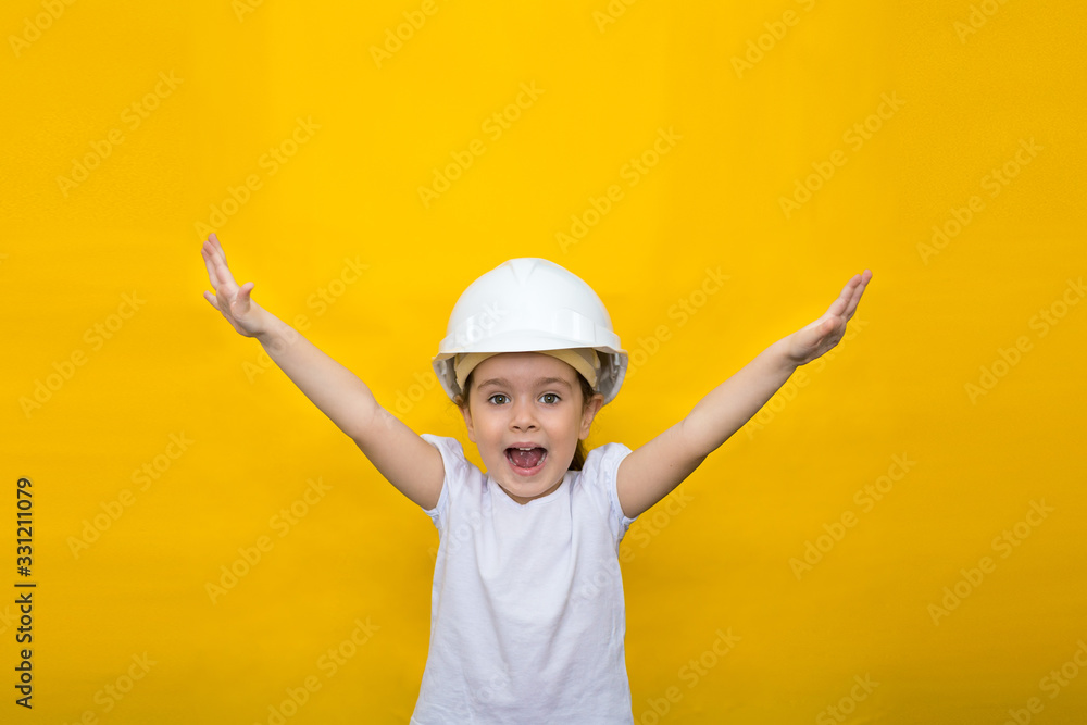 little happy girl in a construction white helmet hands up on a yellow background