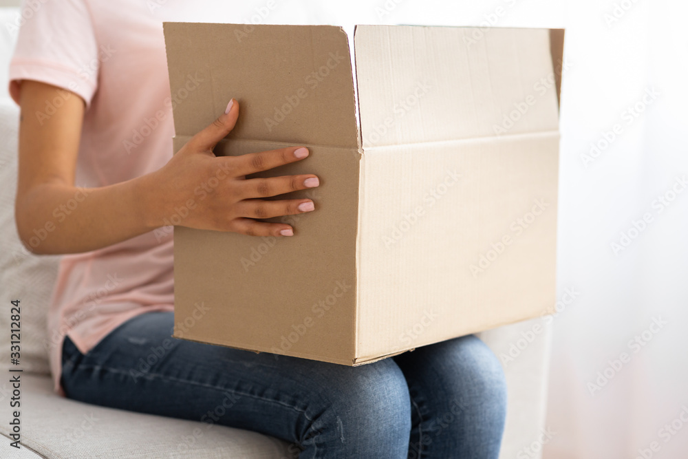 Afro american girl holding a cardboard box on her knees Afro american girl holding a cardboard box on her knees