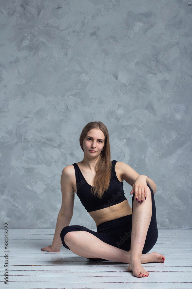 Beautiful athletic young girl sitting on a wooden floor in sports clothes Beautiful athletic young girl sitting on a wooden floor in sports clothes