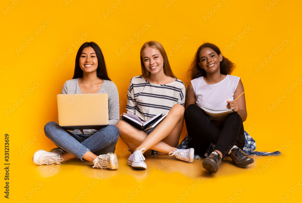 Three students girls studying together, using laptop over yellow background Three students girls studying together, using laptop over yellow background